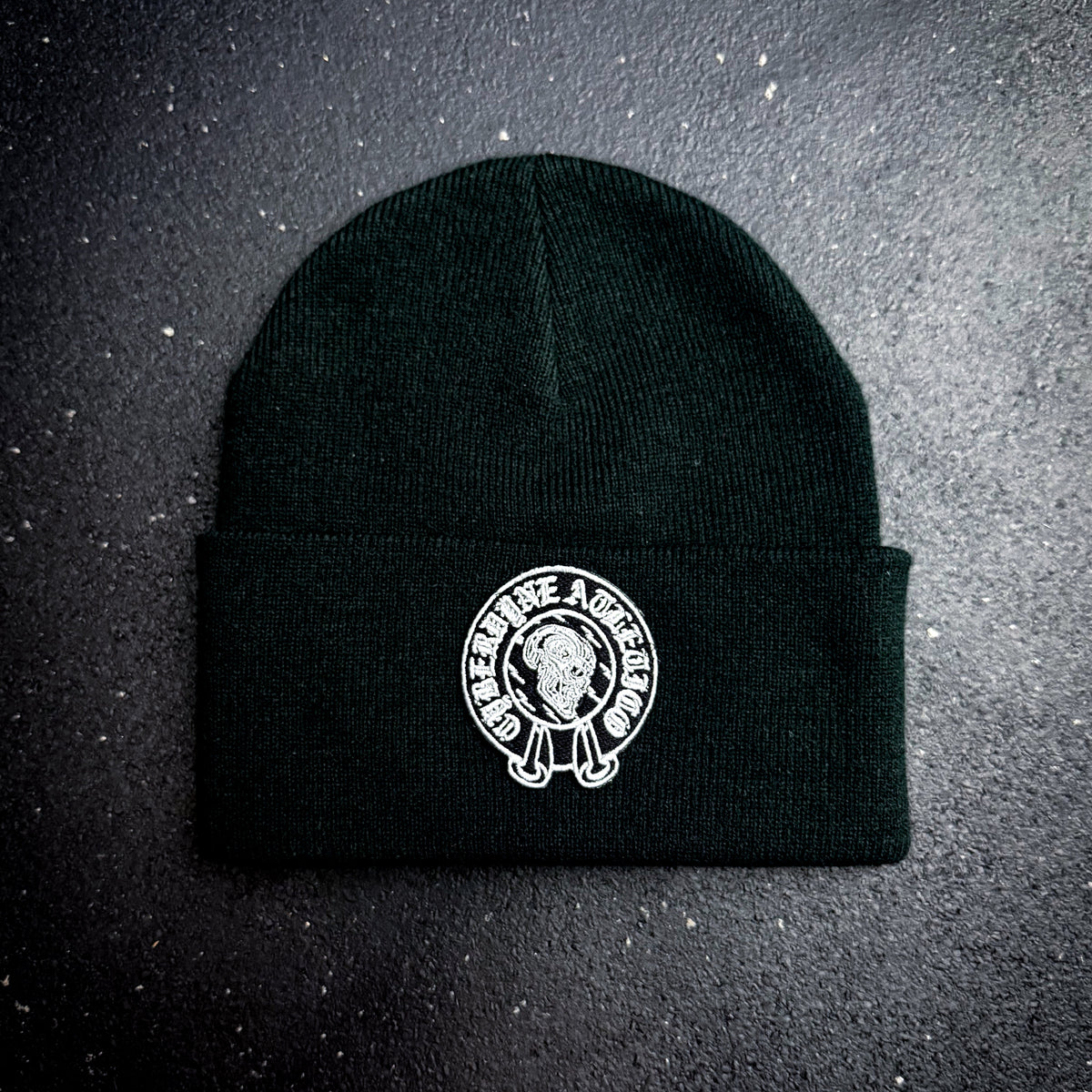 Black beanie with a white cyberdyne atletico chrome hearts style logo on a dark background