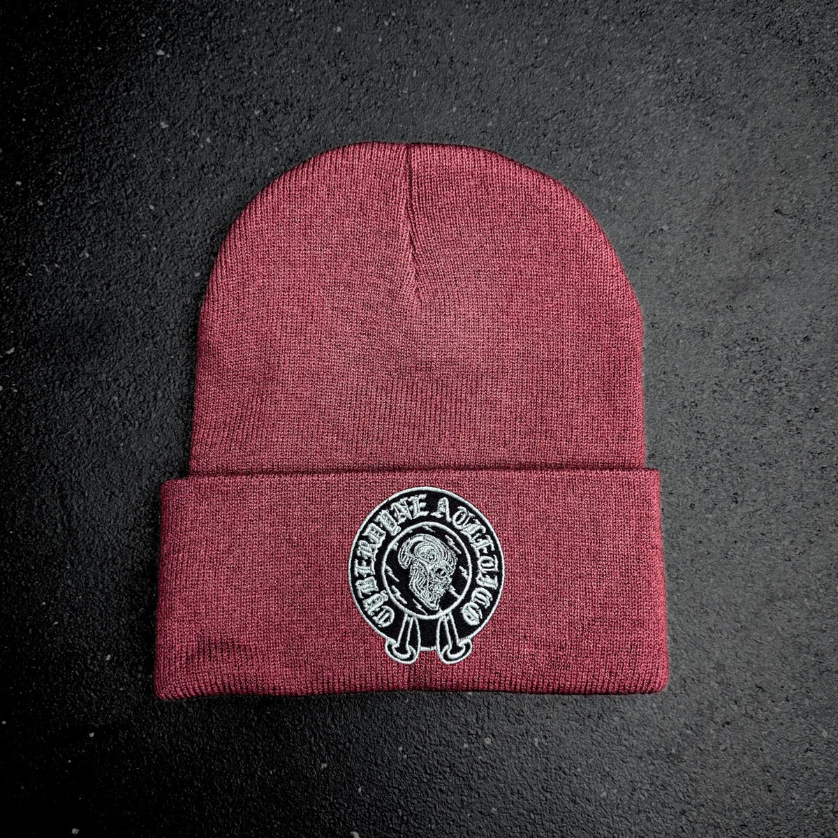 Maroon beanie with a cyberdyne atletico chrome hearts style logo on a black background