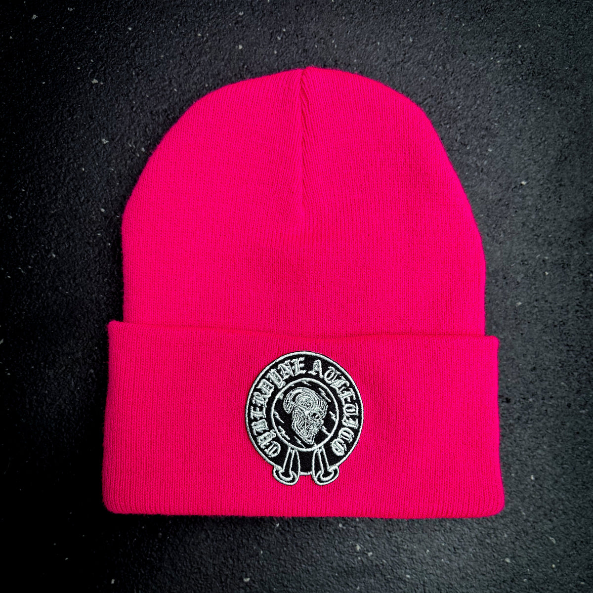 Neon pink beanie with a cyberdyne atletico chrome hearts style logo on a black background